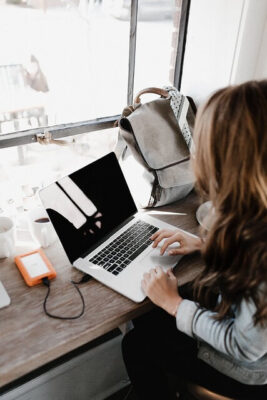 Woman sitting at desk tying on laptop. Has her mobile phone connected to the laptop.