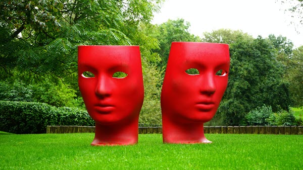 Two face sculptures sitting on lawn.