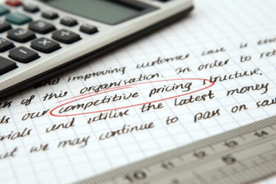 Calculator sitting on top of notepad with words "Competetive Quote" representing RooferQuote.com.