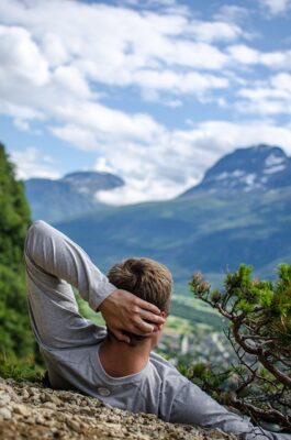 Man laying on back on side of a hill with hand behind head looking at scenery.