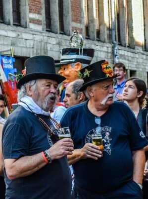Two men in foreground each with a glass of beer. Many people in the background representing festivaltips.com.